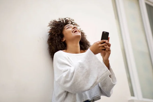 白墙边拿着手机笑的年轻非洲裔美国女人的画像 — 图库照片