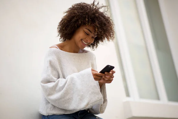 Portrait of smiling african american woman looking at mobile phone outside