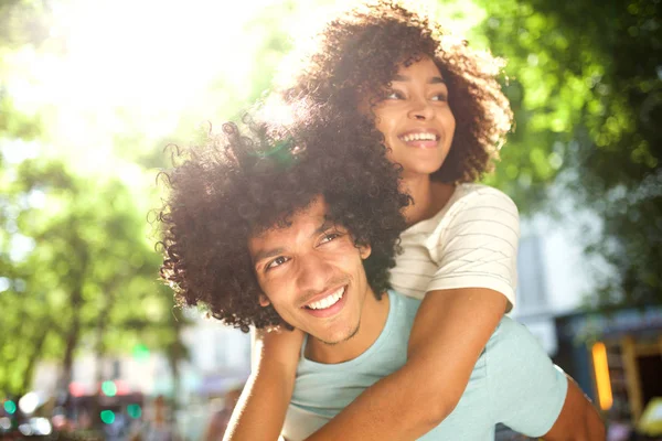 Close up portrait of smiling afro man giving piggyback to happy girlfriend outside