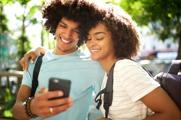 笑顔の若いアフリカ系アメリカ人のカップルの肖像は携帯電話を見て外に立って — ストック写真