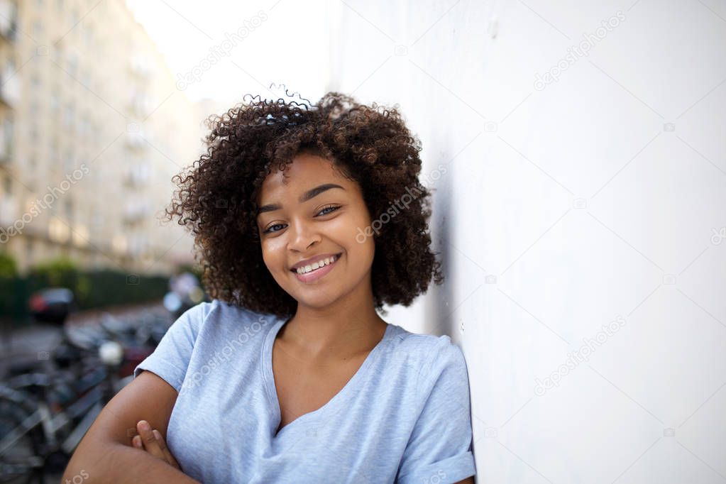 Close up portrait of smiling young african american woman leaning against wall outside