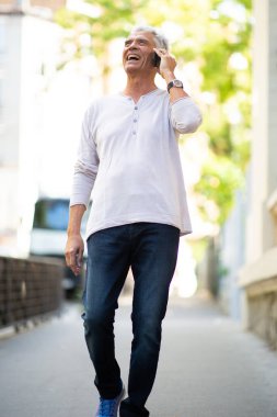 Şehirde yürüyen ve cep telefonuyla konuşan mutlu yaşlı adam portresi