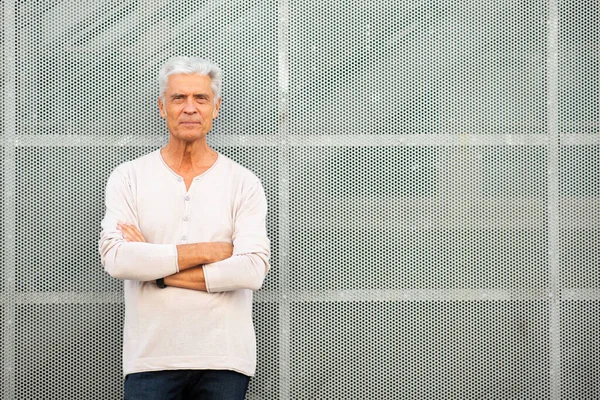 Front portrait handsome older man with arms crossed by wall