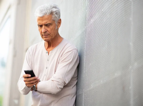 Portret Starszego Mężczyzny Opierającego Się Ścianę Patrzącego Telefon Komórkowy — Zdjęcie stockowe