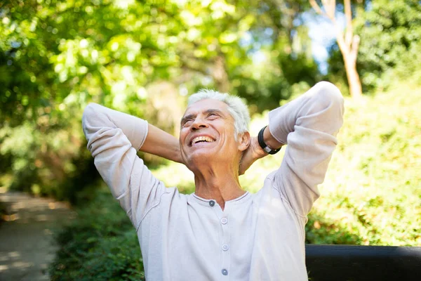 Portrait handsome older man relaxing outside with hands behind head