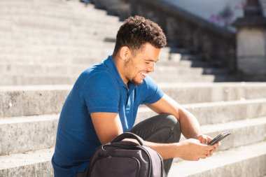 Genç melez ırkın portresi. Merdivenlerde çantasıyla oturmuş cep telefonuna bakıyor.