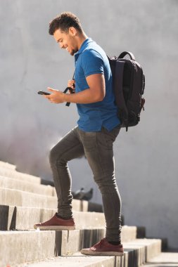 Cep telefonuna bakarak yürüyen mutlu Afro-Amerikan melez bir adamın tam boy portresi.