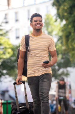 Sokaklarda cep telefonu ve bavulla dolaşan mutlu genç bir adamın portresi.