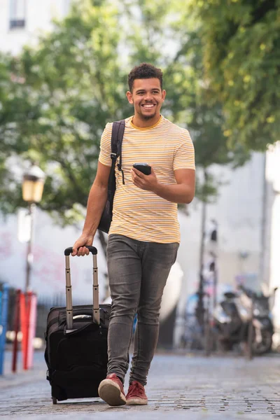 全身ポートレートの幸せな若い男旅行とともに携帯電話とスーツケースオンストリート — ストック写真