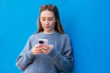 Mavi duvara yaslanan ve akıllı telefon kullanan kadın