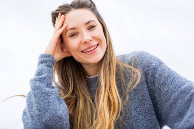 Rahatlamış genç bir kadın, eli başının üstünde gülümsüyor.