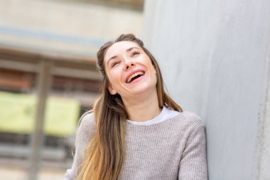 Açık havada duvara yaslanan mutlu genç kadın.