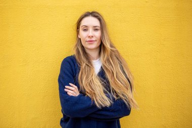 Sarı duvara karşı kollarını kavuşturmuş kendine güvenen bir kadın.