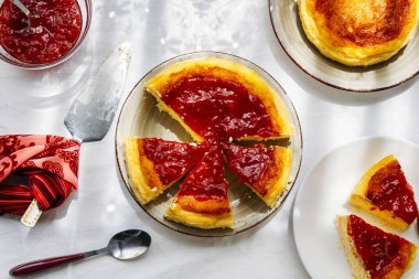 Ev yapımı peynirli kek reçelle süslenmiş ve sıcak ve güneşli bir günde güneş ışığının içeri girdiği pencerenin yanındaki dilimlere bölünmüş. Sağlıklı, ev yapımı tatlılar.