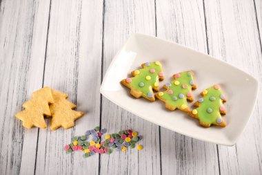 Yeşil kremalı kurabiyelerle süslenmiş zencefilli kurabiyelerden yapılmış lezzetli Noel ağaçlarının ve kırsal ahşap masa simülasyonu yapan renkli şekerli konfetilerin üst görüntüsü. Noel tatlısı