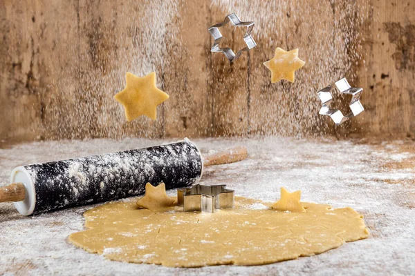 Raw star-shaped ginger cookies fall through the air with flour and cutters on a floured wooden table and a rolling pin. Concept of flying and fun food. Christmas desserts.