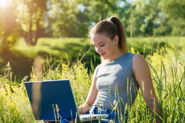 bir dizüstü bilgisayar açık havada yeşil çim arasında oturan kız. Internet üzerinden iletişim kurar.