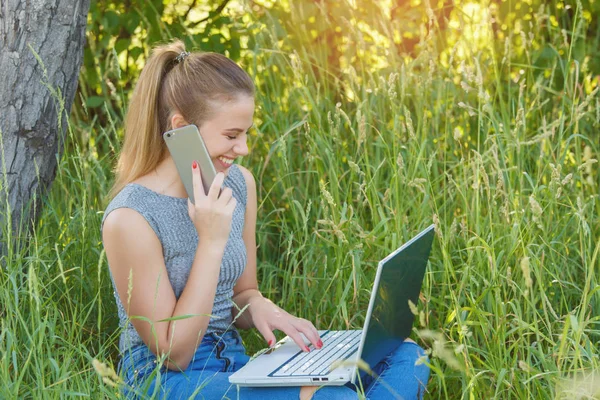 Κορίτσι με ένα φορητό υπολογιστή που μιλάει στο τηλέφωνο στη φύση — Φωτογραφία Αρχείου