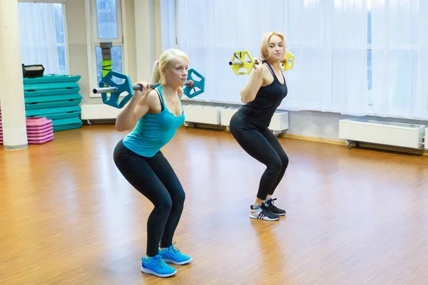 Zwei Athletinnen halten die Stange auf seinen Schultern. Mädchen machen Kniebeugen in der Turnhalle, Fitnessraum. — Stockfoto