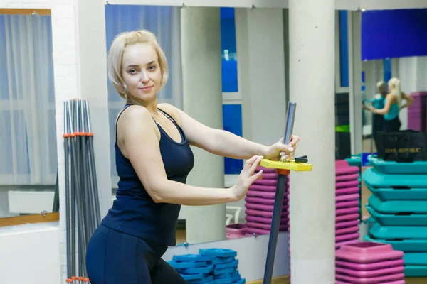 Una joven sosteniendo una bomba de fitness, preparándose para hacer ejercicio en el gimnasio. Ella mira el bar y se ajusta para realizar ejercicios deportivos . — Foto de Stock