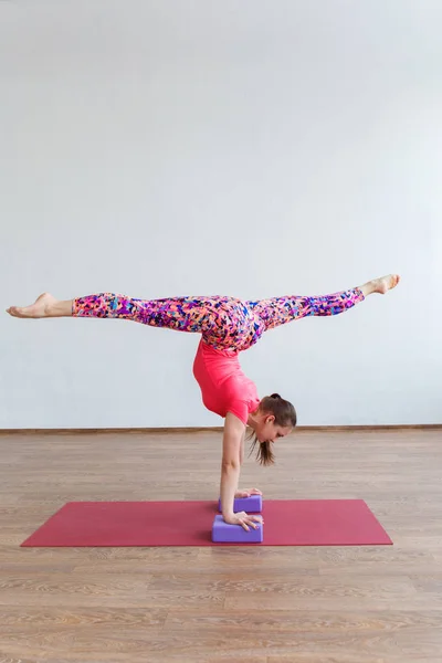 A young gymnast girl stands on her hands with her legs bent at the top. — Stock Photo, Image