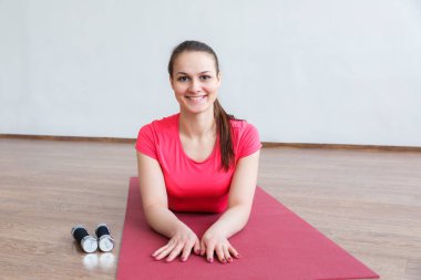 Fitness sonra güzel bir gülümseme ile genç bir kız mat yatıyor. Kız ve dambıl.