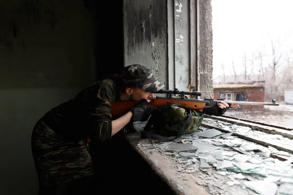 Kız keskin nişancı kapsam üzerinden bakar. Kız savaşçı terk edilmiş bir binanın kırık penceresinden tüfeğini yönlendirir. Kızlar için askerlik hizmeti.