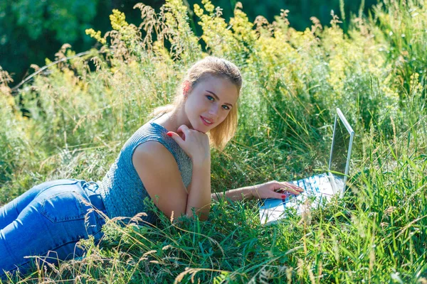 Girl with a laptop in nature lying on the grass. The concept of combining leisure and work. Individual entrepreneur. Work at the computer away from the city.