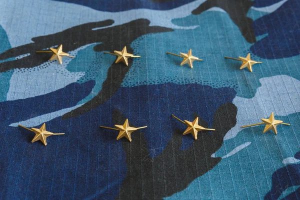 Gold stars for shoulder straps on blue camouflage fabric. Military emblems of Russian troops and services. No people