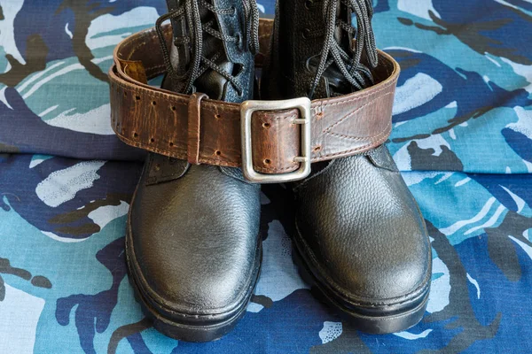 Army boots and army belt on blue camouflage fabric. Overalls for the soldier.