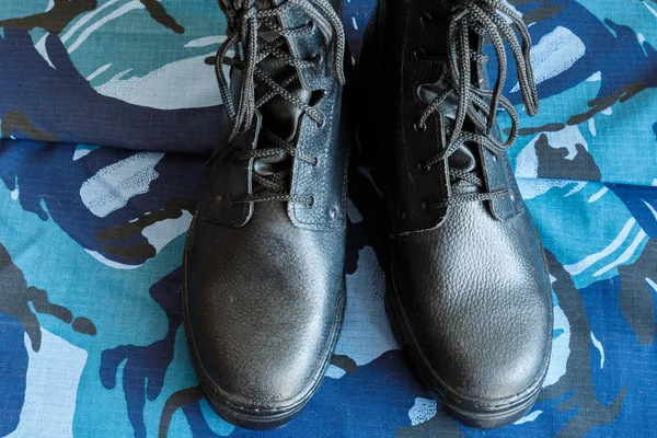 A pair of black army boots on fabric with blue camouflage . No people. Army boots for the soldier. The front part of the Shoe.