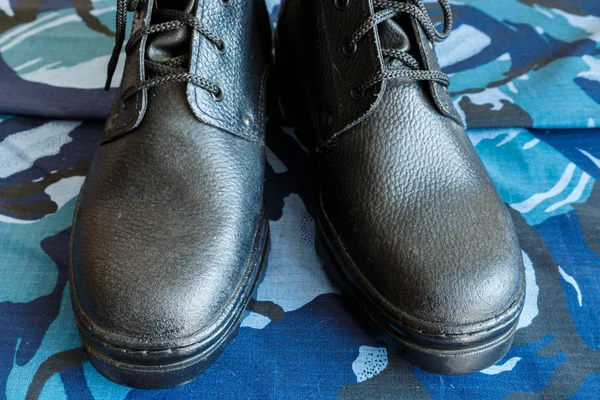Pár černých armádních bot na tkanině s modrou kamufláž. Žádní lidé. Armádní boty pro vojáka. Přední část obuvi. — Stock fotografie