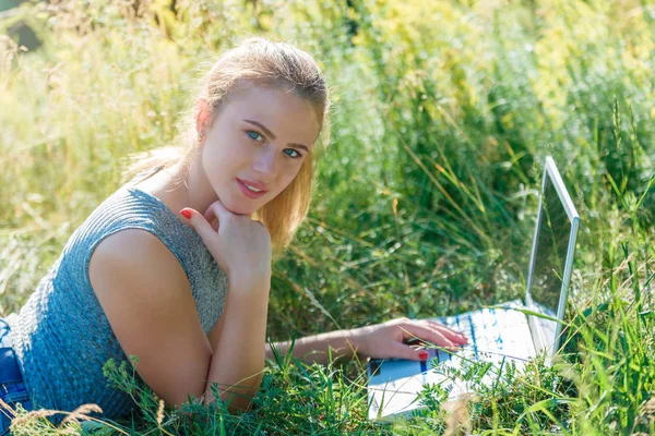 A girl with a laptop in nature lying on the grass with sunlight. The concept of combining leisure and work. Individual entrepreneur. Work at the computer away from the city.