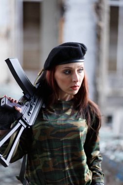 Harabeler arasında yeşil kamuflaj üniformalı ve silahı olan siyah bereli genç bir kız. Silah ile kız savaşçı.