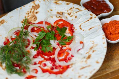 Kırmızı biber, soğan, nar ve maydanoz lavaş üzerine kavrulmuş et, sosis veya sosis ketçap ve Ermeni çerez Aivar ile servis edilir. Yukarıdan görünüm.