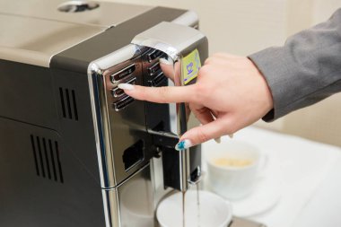 Kız kahve makinesinde kahve yapma modu seçer. Kadın el kahve makinesinin düğmesine basar .