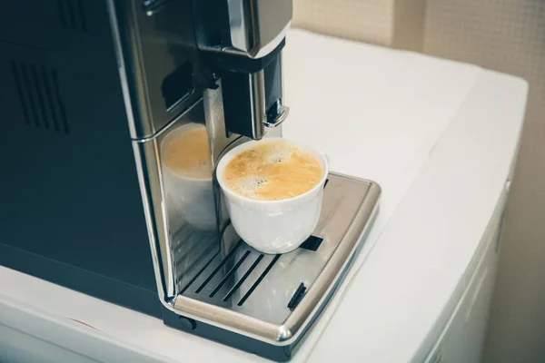 Кавовий автомат наливає свіжозварену каву в білу чашку. Кава з пінополіуретану. — стокове фото