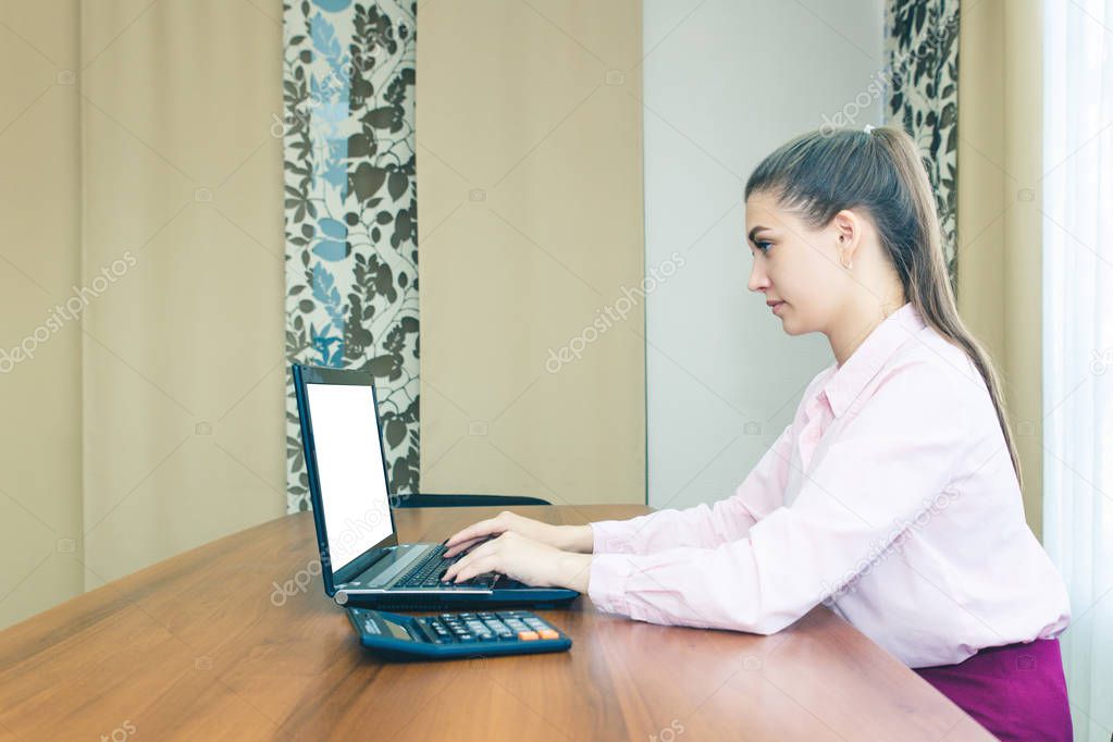 The girl in the workplace in the office with a laptop. Laptop with white blank screen. Side view.