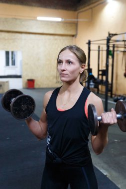 Spor salonunda dambıllı kız atlet. Kız halterile egzersiz yapar.