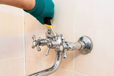 Bir İngiliz anahtarı ile eldivenli el banyoda musluk tamir.