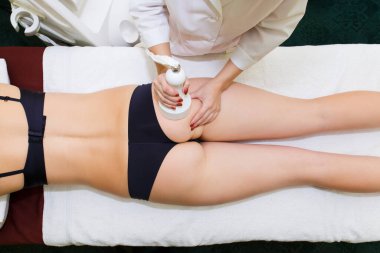 Bir kadın güzellik uzmanı ultrasonik boşluğu olan bir kadına anti-selülit masajı yapıyor. Yukarıdan görüntüle.