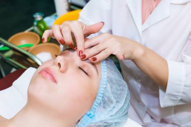 Masör parmaklarıyla yüzün aküpres masajını yapıyor. Parmak masajıyla yüz yenileme prosedürü.