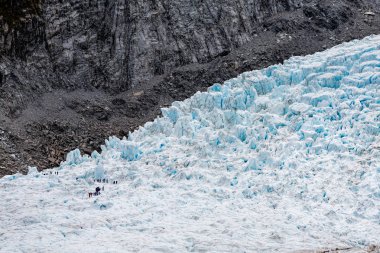 Grup alt sol köşedeki yürüyüşçü Franz Josef Glacier, south Island Yeni Zelanda siyah gri taşın karşı bitişik mavi buz üzerinde ölçek duygusu eklemek