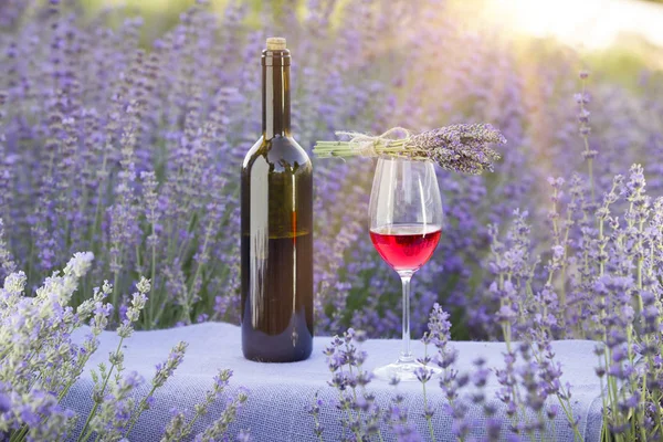 Rotweinflasche und Weinglas auf dem Tisch. Weinflasche gegen Lavendellandschaft. Sonnenuntergang über einem sommerlichen Lavendelfeld in der Provence, Frankreich — Stockfoto