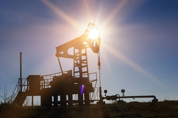 Silhouette pompa olio di lavoro contro sole e cielo blu — Foto Stock