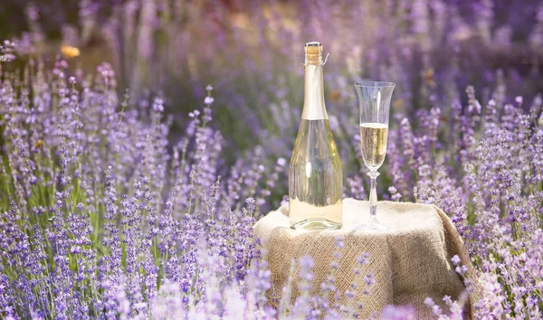 Champagnerflasche und Weinglas auf dem Tisch. Flasche Alkohol gegen Lavendellandschaft. Sonnenuntergang über einem sommerlichen Lavendelfeld in der Provence, Frankreich — Stockfoto