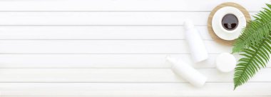 Eğrelti otu yaprakları ve yatay panellerle kahve fincanı manzarası. Yeşil eğrelti otunun dekorasyon arka planında siyah kahve bardağıyla krema ve şampuan şişesinin spa kompozisyonu.