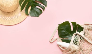 Pembe arka planda tropik palmiye yaprağı ve eko torba. Canavar yapraklarıyla birlikte güneş kremi ve şapka. Çok az moda konsepti..