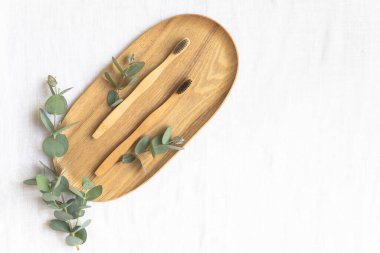 Bambool diş fırçası ve okaliptüs yaprakları ahşap tabakta.