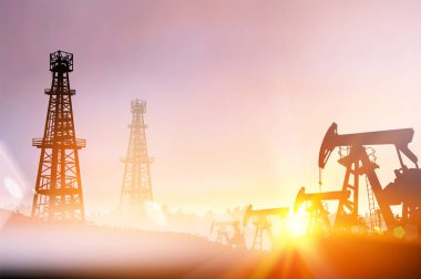 Gün batımında petrol kulesi ve pompaların siyah silueti